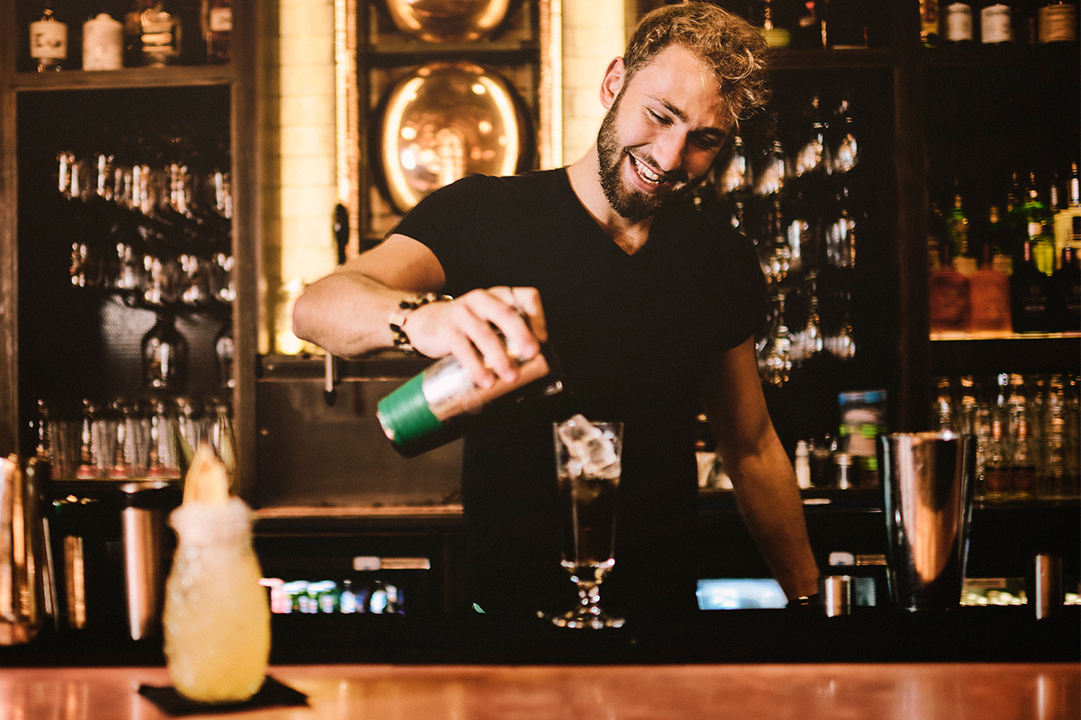 A bartender pouring a cocktail into a glass.
