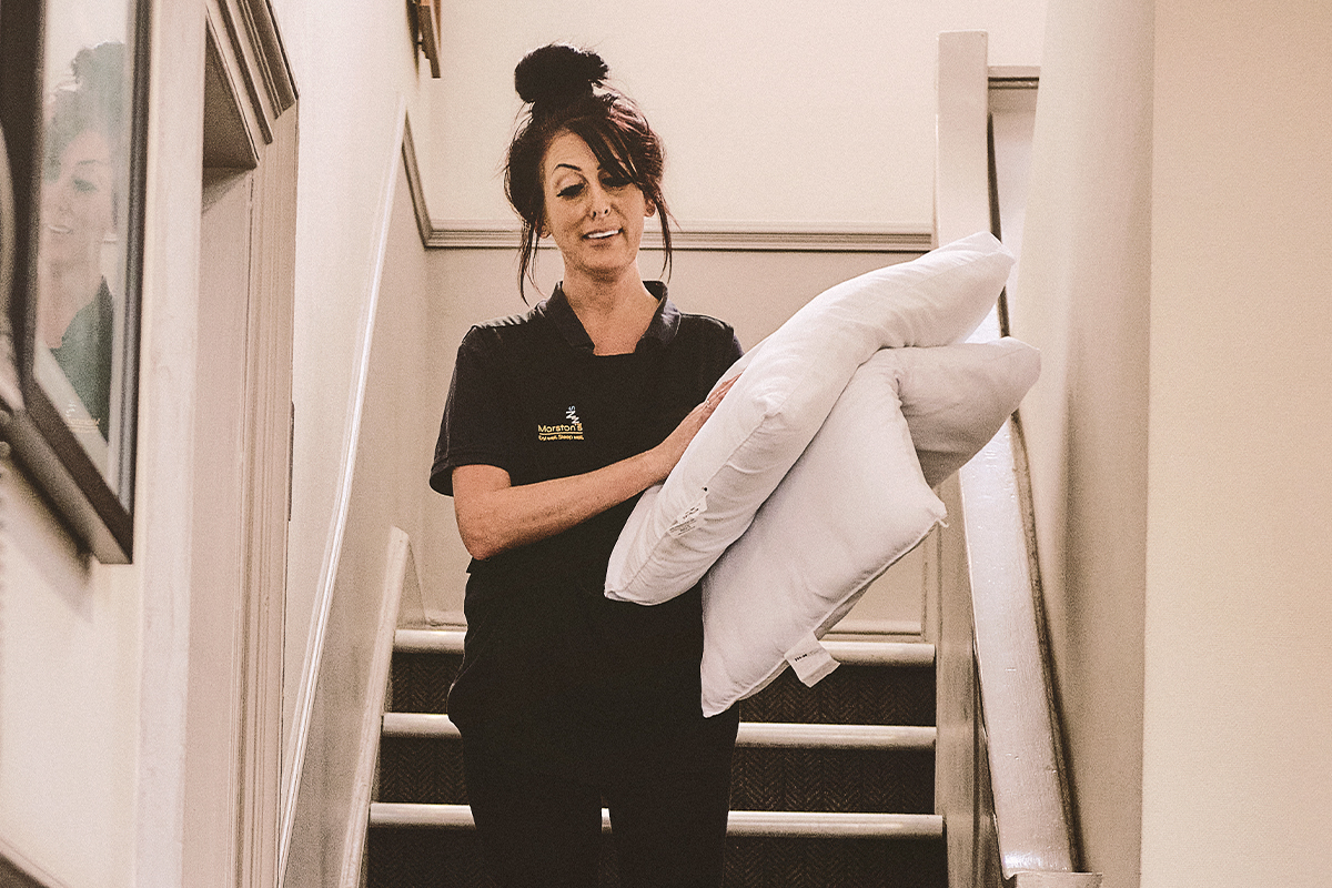 A cleaner is carrying pillows down to a guest room as she preps for a new arrival.