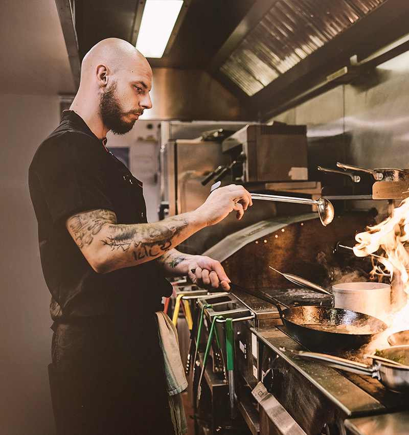 Chef in a pub kitchen preparing food in a pan.