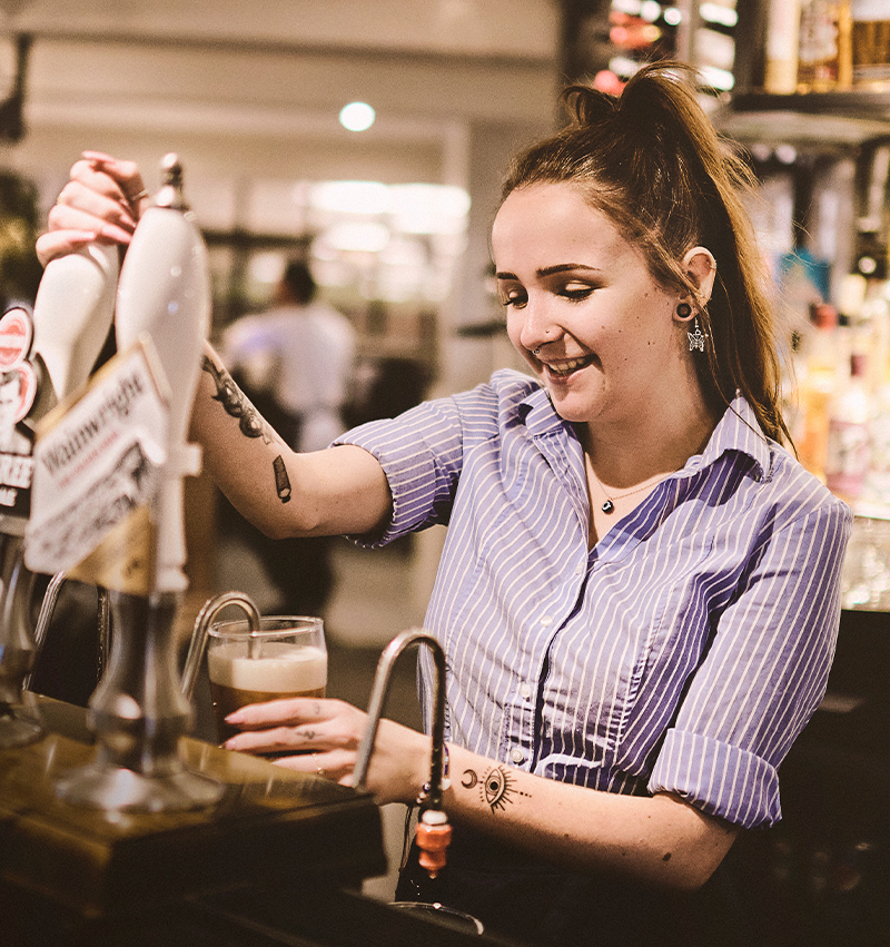 Bartender pulling a pint and smiling as she gets ready to hand it over to a guest.